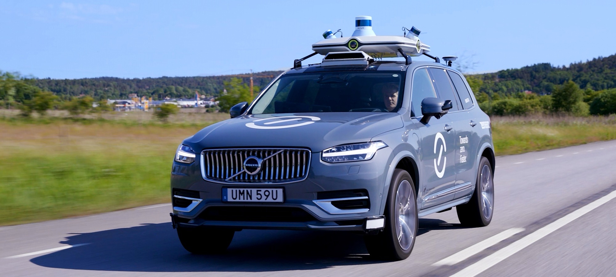 Zenseact car with sensors on top, on the road, green scenery in the background